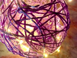 Up close shot of purple acrylic yarn globe with warm colored faery lights