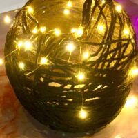 Close up of a black and gold colored acrylic yarn globe with warm colored faery lights