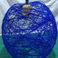 Yarn globe pendant lamp made out of blue cotton yarn with a gold colored hanging lamp holder